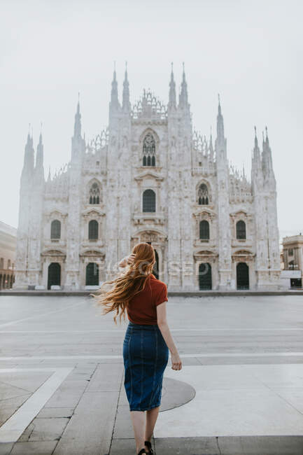 Back view of anonymous female tourist with flying hair on pavement against old masonry cathedral with decor in Milan Italy — Stock Photo