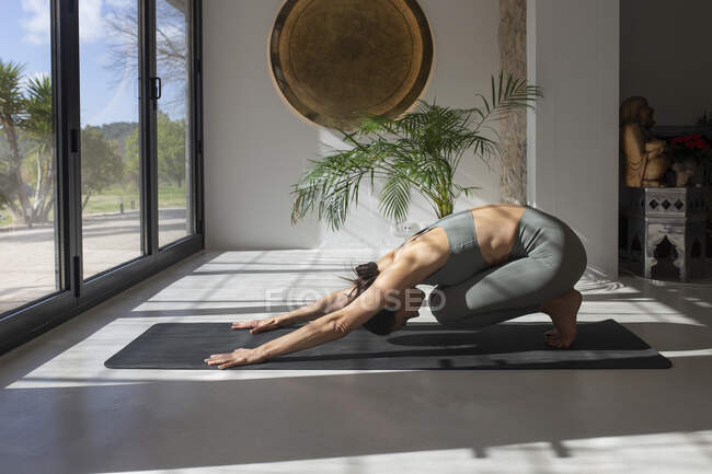 Vista lateral de la pacífica hembra en ropa deportiva practicando yoga en pose infantil mientras estira el cuerpo - foto de stock