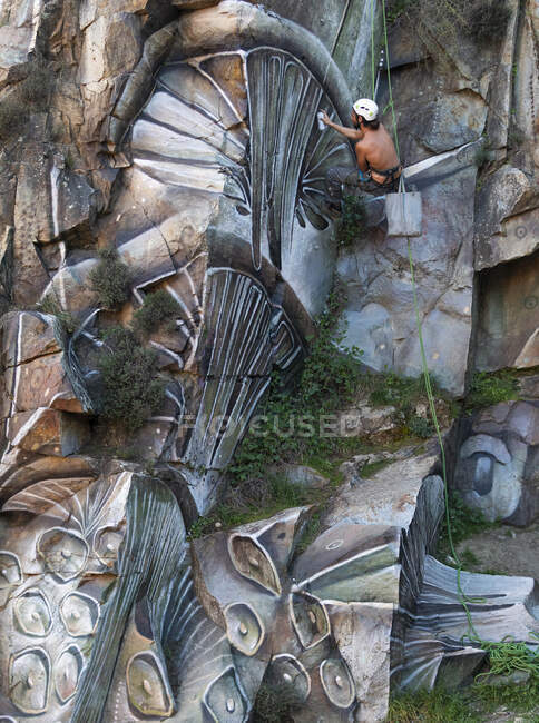 Side view full body of painter with spray paint making graffiti hanging on rope on steep rocky slope — Stock Photo