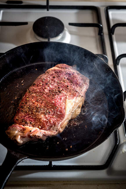 De cima da panela com a parte de carne apetitosa com condimentos e na manteiga derretida no fogão a gás — Fotografia de Stock