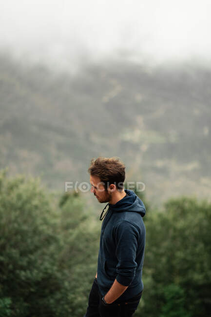 Vue de côté randonneur masculin réfléchi debout sur le sommet de la montagne dans les hauts plateaux de Séville par temps nuageux et brumeux — Photo de stock