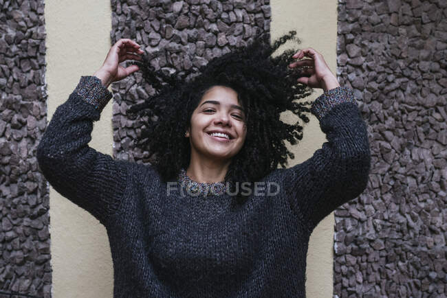 Entzückte ethnische Frau mit Afro-Frisur, die auf der Straße steht und lockiges Haar berührt, während sie in die Kamera schaut — Stockfoto