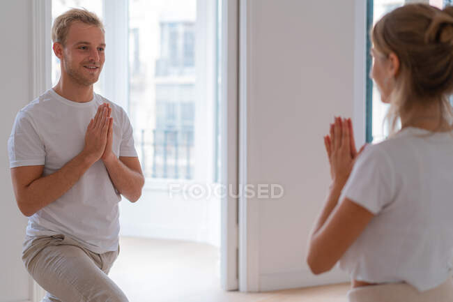 Seitenansicht eines zufriedenen Paares in Aktivkleidung, das auf Matten in Anjaneyasana steht, mit namaste Geste, während es morgens Yoga macht und sich gegenseitig ansieht — Stockfoto