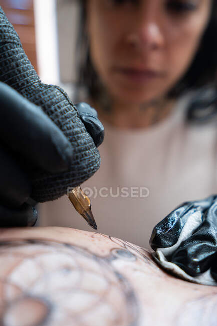 Female tattooer with machine drawing tattoo on body of unrecognizable client in salon — Stock Photo