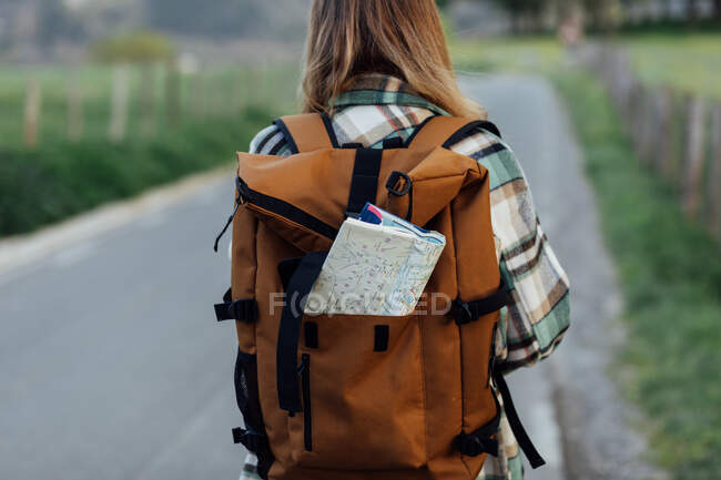Вид ззаду анонімна жінка-пішохідка з картою маршруту в рюкзаку на проїжджій частині в сільській місцевості — стокове фото