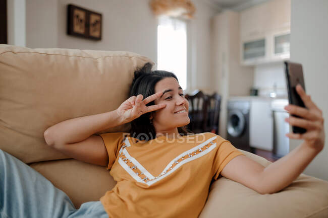 Young female taking self portrait on cellphone while lying down on couch in living room — Stock Photo