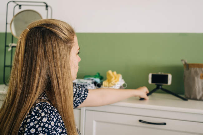 Вид збоку молодої жінки-блогера з коричневим волоссям і мобільним телефоном на комоді в кімнаті легкого будинку — стокове фото