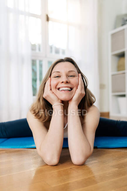 Charmoso encantado feminino alongamento pernas em Split asana enquanto pratica ioga em casa e olhando para a câmera — Fotografia de Stock