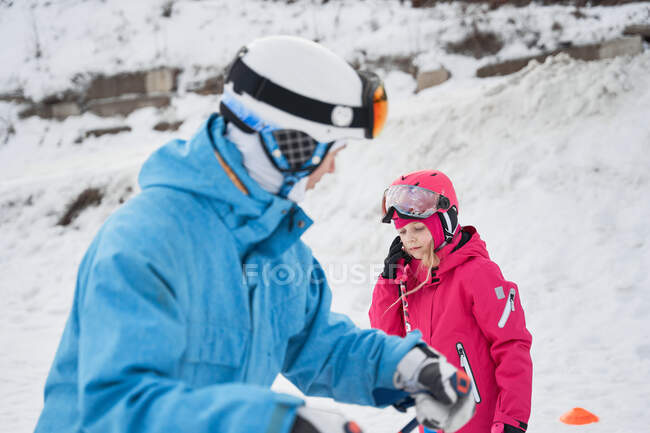 Pais em roupas esportivas quentes e capacete ensinando criança a esquiar ao lado de encostas nevadas na estação de esqui de inverno — Fotografia de Stock