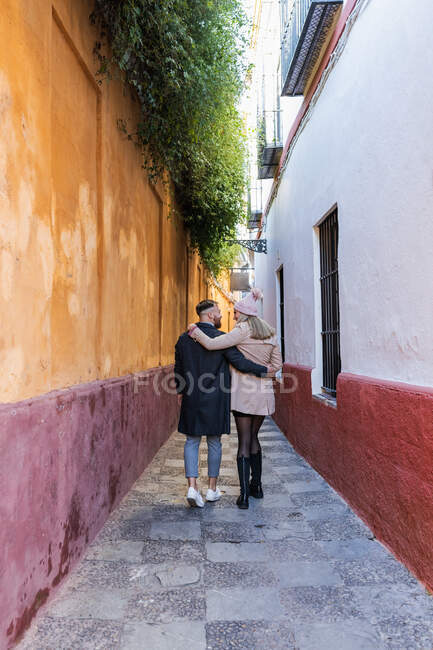 На задньому плані подружжя закоханих у зовнішні убори обіймає і йде по старій вузькій вулиці, насолоджуючись прогулянкою в місті і дивлячись один на одного. — стокове фото