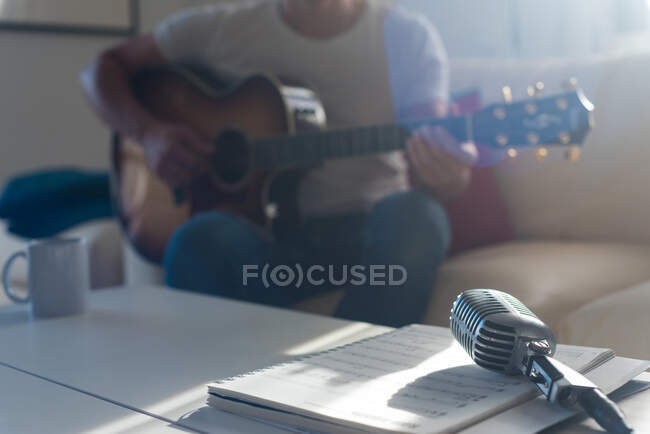 Винтажный микрофон, установленный на столе возле урожая, неузнаваемый бородатый мужчина-музыкант, играющий на акустической гитаре на диване — стоковое фото