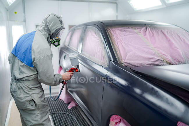 Side view of male in respiratory mask and protective suit painting car with spray gun in service — Stock Photo
