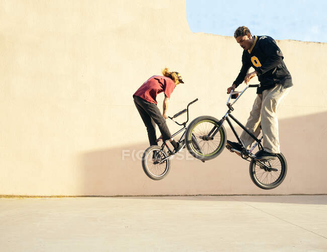 Side view of young multiethnic male athletes jumping on BMX bicycles during training over pavement — Stock Photo