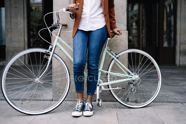 Crop black woman in smart casual style standing along street with bike — Stock Photo