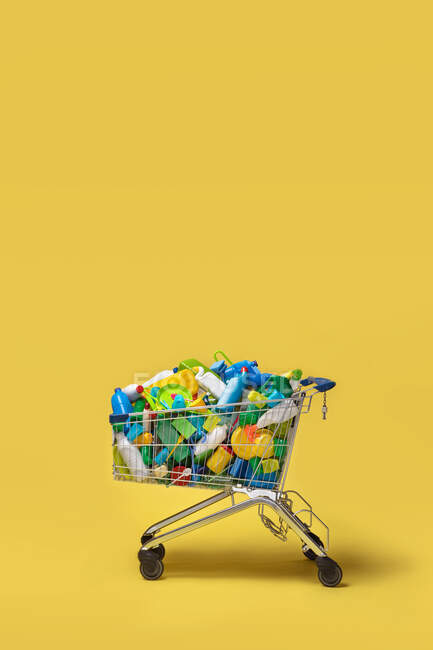Warenkorb mit diversen bunten Plastikverpackungen auf gelbem Hintergrund — Stockfoto