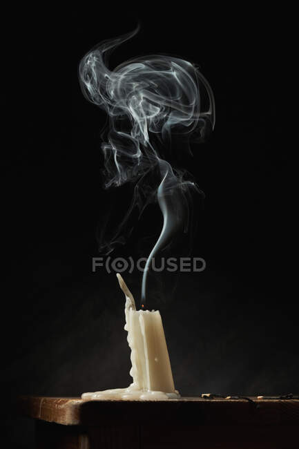 Fumaça sobre vela extinta branca colocada na mesa de madeira no fundo preto no estúdio — Fotografia de Stock