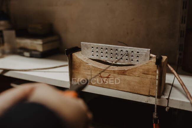 Руки анонимного ювелира, вытаскивающего гибкую металлическую палку через отверстия во время изготовления украшений в мастерской — стоковое фото