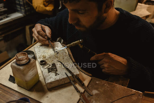 Bärtiger Goldschmied mit Zange bei der Herstellung winziger Metalldetails auf Werkbank in Werkstatt — Stockfoto