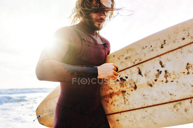 Surfer man dressed in wetsuit running with surfboard on the beach during sunrise — Stock Photo
