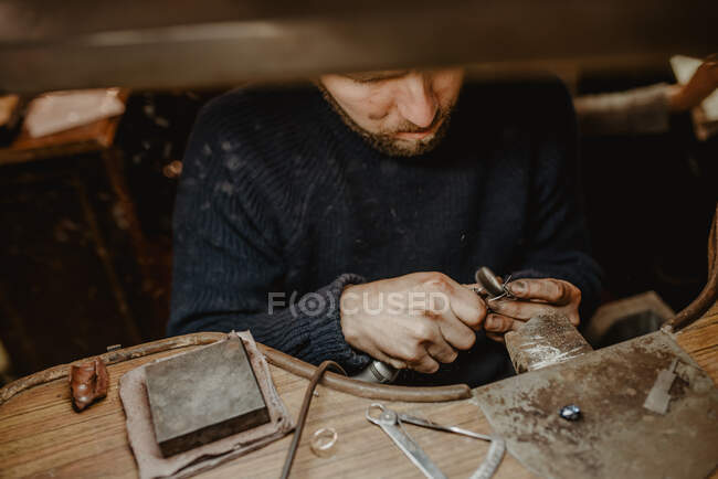 Bijoutier utilisant une machine de polissage professionnelle sur établi tout en faisant une bague en métal dans l'atelier — Photo de stock