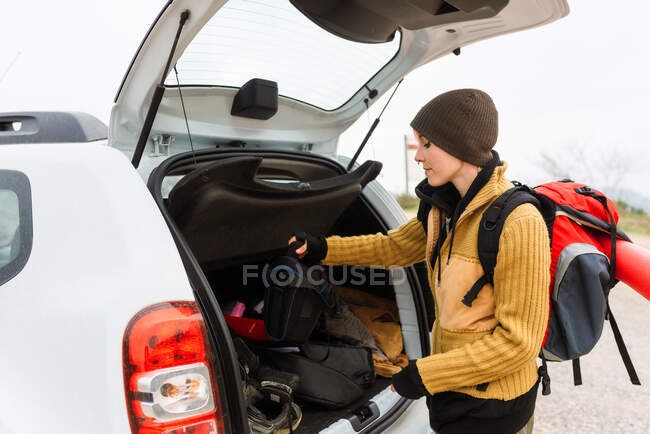 Side view of content female adventurer standing with traveling backpack near car trunk in mountains — Stock Photo
