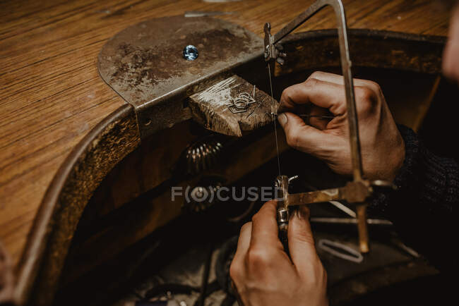 Orfèvre découpe le métal avec une scie lors de la fabrication de bijoux en atelier — Photo de stock