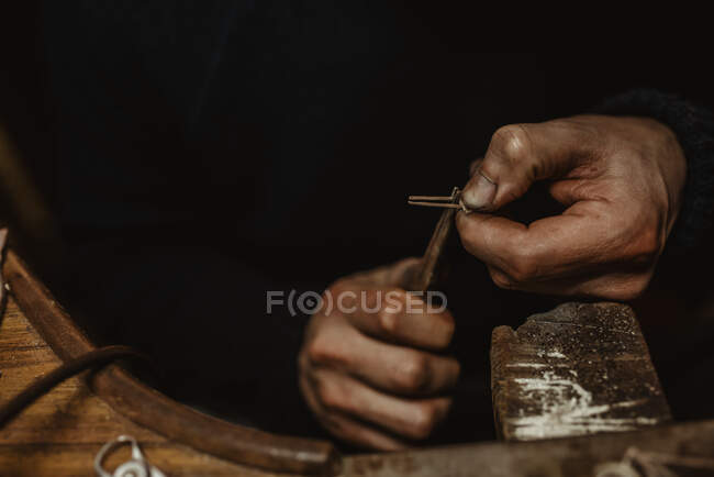 Orfèvre masculin barbu utilisant des pinces tout en faisant de minuscules détails métalliques sur l'établi en atelier — Photo de stock