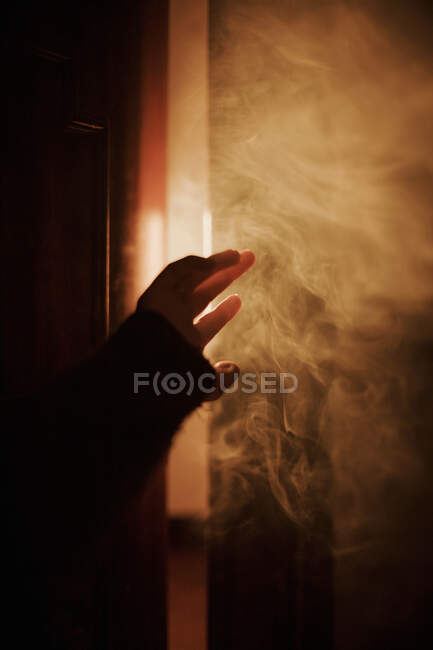Erhobene Hand einer gesichtslosen Person in dunklem Studio mit Rauch, der mit hellem Licht beleuchtet wird — Stockfoto