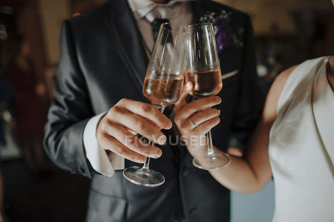 Crop anonymous bride and groom in elegant wedding clothes clinking wineglasses with champagne during celebration — Stock Photo