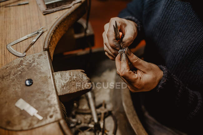Anónimo joyero sosteniendo anillo inacabado en manos sucias y comprobando la calidad en el taller - foto de stock