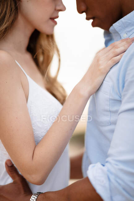 Vue latérale d'un couple multiracial amoureux de jeunes mariés embrassant tout en se tenant debout sur une colline sablonneuse sur fond de mer le jour du mariage — Photo de stock