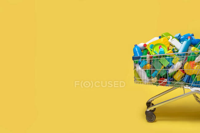 Carro de diversos paquetes de plástico de colores sobre fondo amarillo - foto de stock