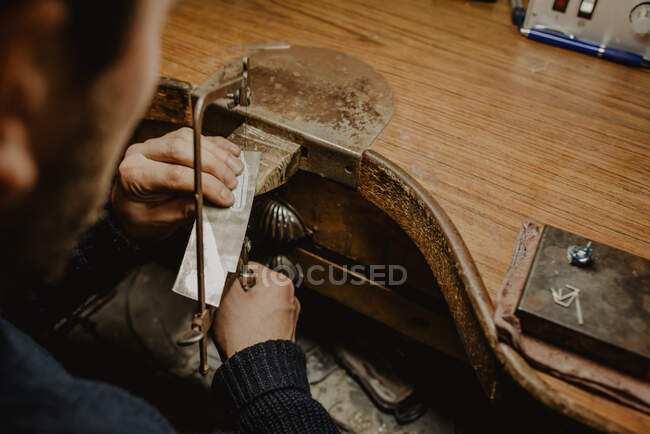 Unrecognizable goldsmith cutting metal with saw while making jewellery in workshop — Stock Photo