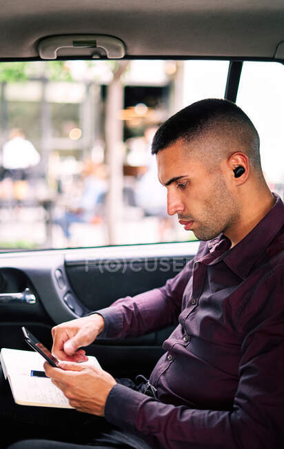 Entrepreneur hispanique concentré assis sur le siège passager de la voiture et écrivant dans le planificateur tout en se rendant au travail — Photo de stock