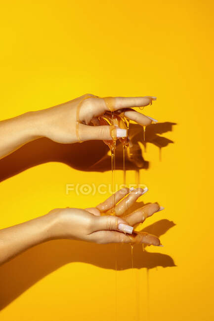 Cultivo femenino irreconocible mostrando mano con manicura y fluidos aromáticos de miel sobre fondo amarillo con sombra - foto de stock