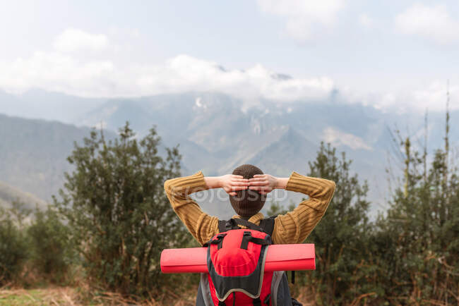 Vista posteriore di esploratore anonimo con zaino in piedi con le mani dietro la testa e godendo di libertà durante il viaggio in montagna — Foto stock