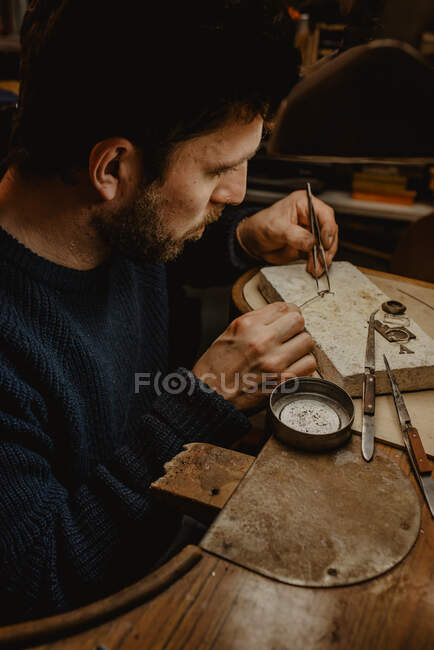 Manos de Goldsmith cortando metal con sierra mientras hace joyas en taller - foto de stock