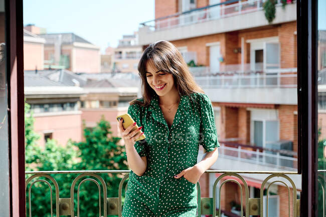 Cheerful female browsing mobile phone while standing on balcony on sunny day — Stock Photo