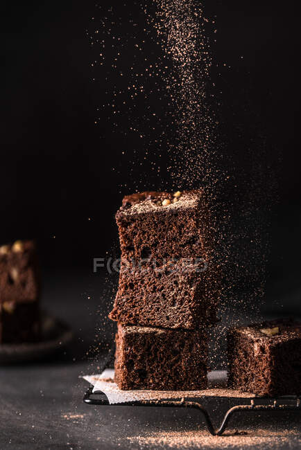 Composição de pequena pilha de saborosos cortes de brownie doce com pó no fundo preto — Fotografia de Stock