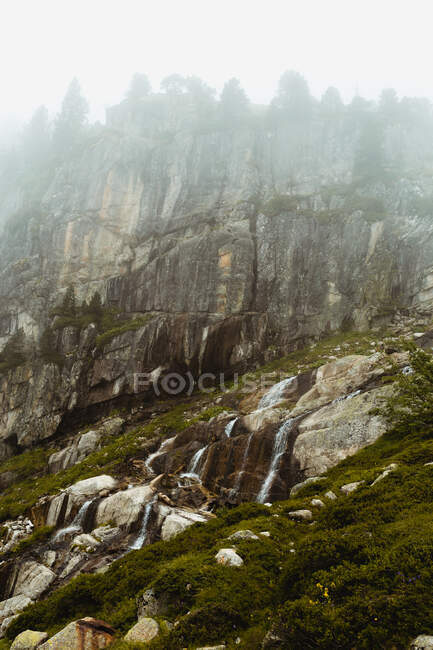 Мальовничий вид на зелені скелі на пагорбі біля лугу з травою і хмарним небом — стокове фото