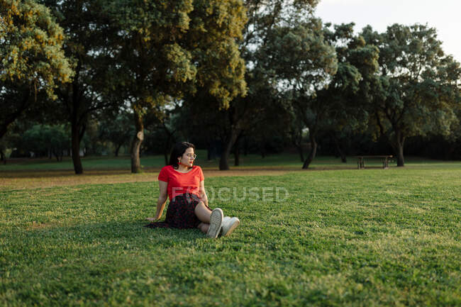 Tranquil female sitting on grass on meadow in park and enjoy sunset in summer — Stock Photo
