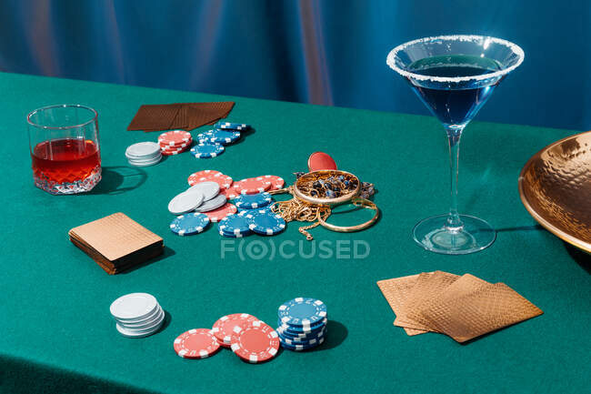 Green poker table with cards and chips placed near jewelry and glasses with alcohol cocktails — Stock Photo