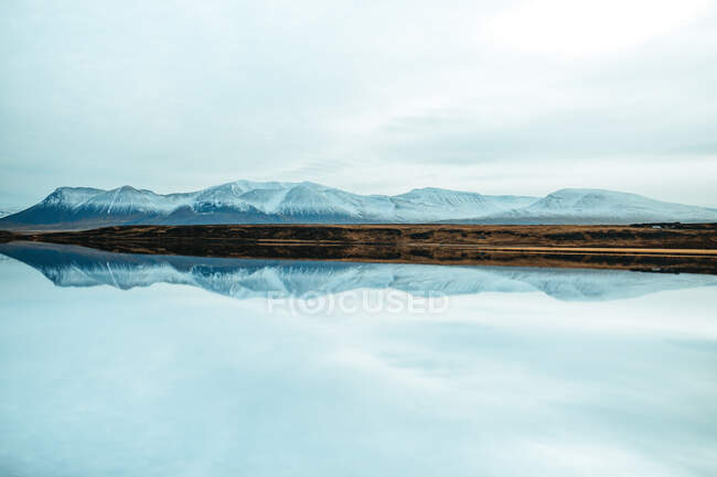 Vue pittoresque de la surface de l'eau près de collines rocheuses étonnantes dans la neige et le ciel bleu — Photo de stock