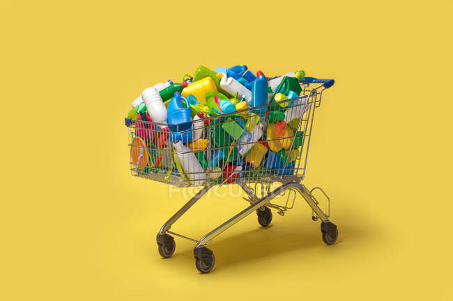 Carrinho de diversos pacotes de plástico colorido sobre fundo amarelo — Fotografia de Stock