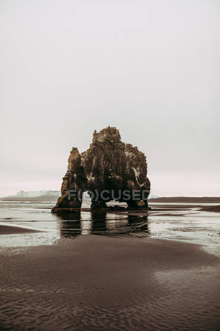 Incredibile enorme roccia alta tra la costa di sabbia con acqua e cielo nuvoloso — Foto stock