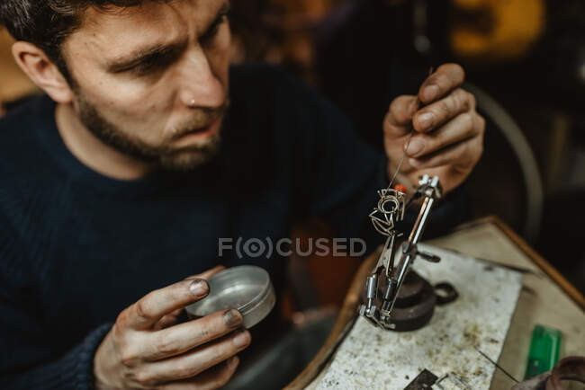 Goldsmith using blowtorch to heat tiny metal ornament while making jewellery on workbench — Stock Photo