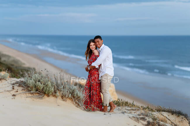 Loving multiracial couple in elegant clothes embracing on hill on background of evening in summer — Stock Photo