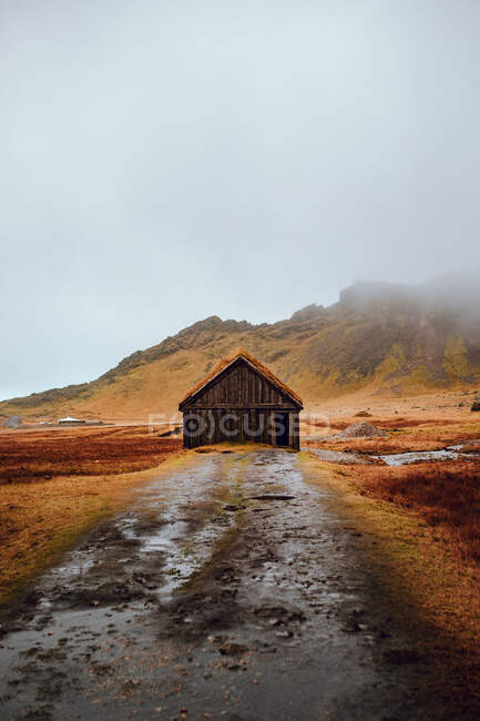 Cabaña envejecida entre tierras salvajes cerca de altas colinas de piedra y cielo nublado - foto de stock