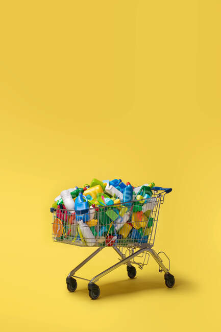 Carrello di diverse confezioni di plastica colorata su sfondo giallo — Foto stock