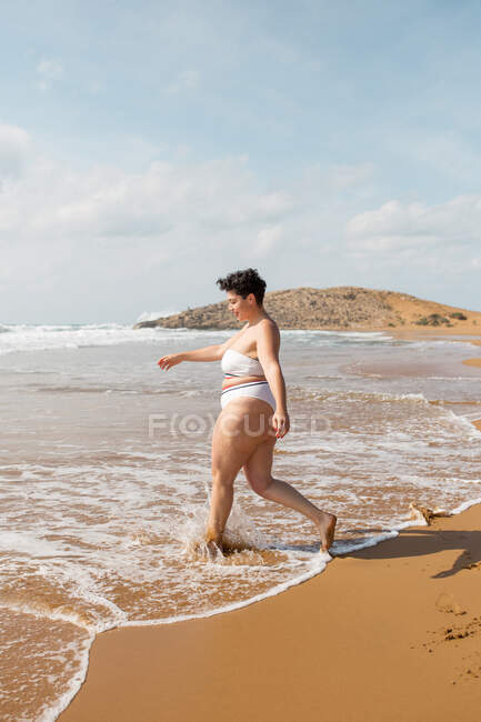 Junge Frau im Badeanzug steht an der Sandküste bei sonnigem Tag unter blauem bewölkten Himmel — Stockfoto